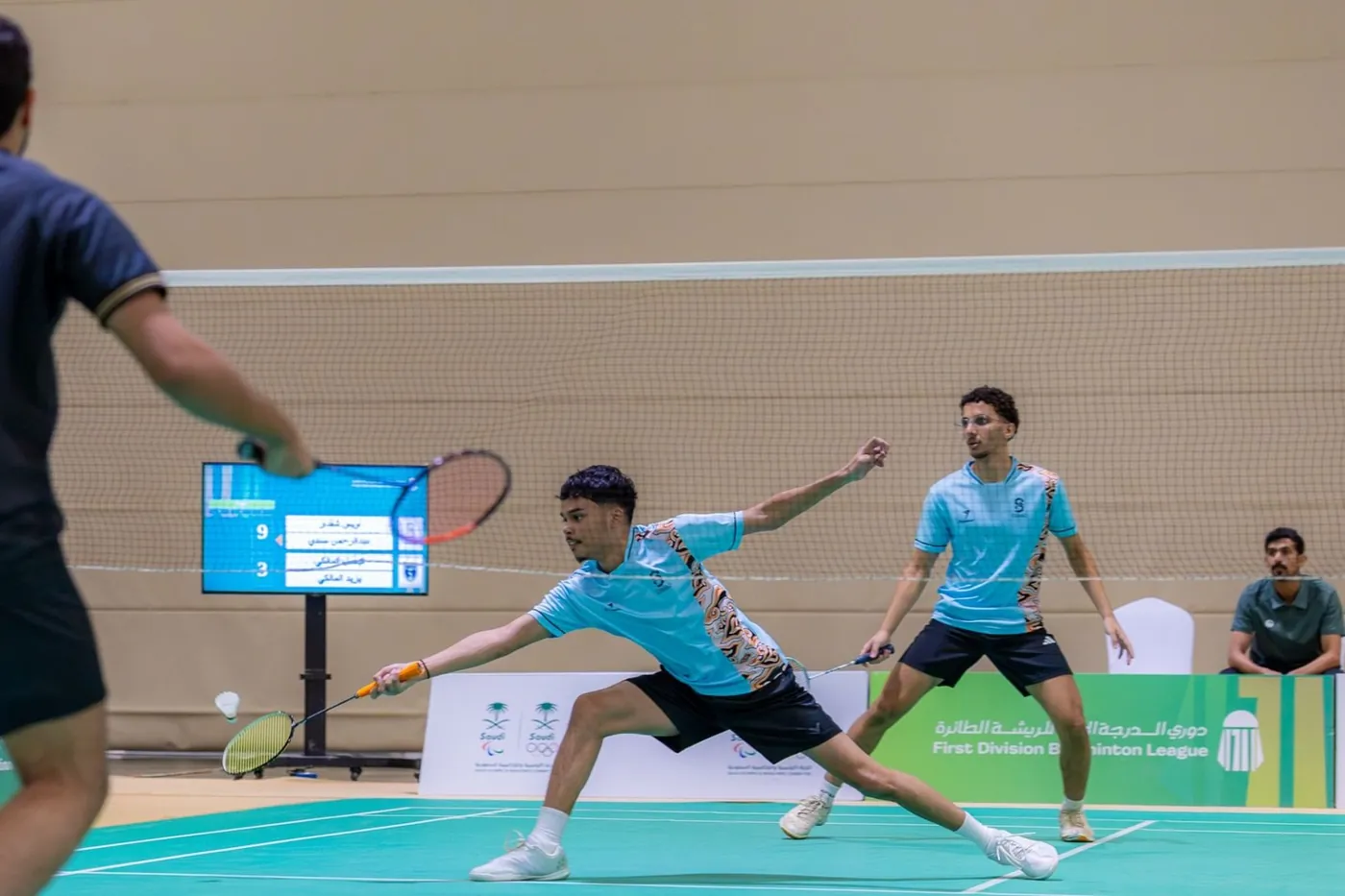 Игроки в парном разряде тянутся за воланом на корте Saudi Badminton Federation
