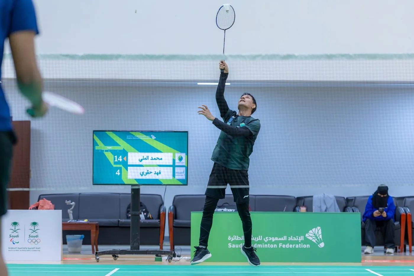 Игрок подаёт рядом с live-табло на мероприятии Saudi Badminton Federation